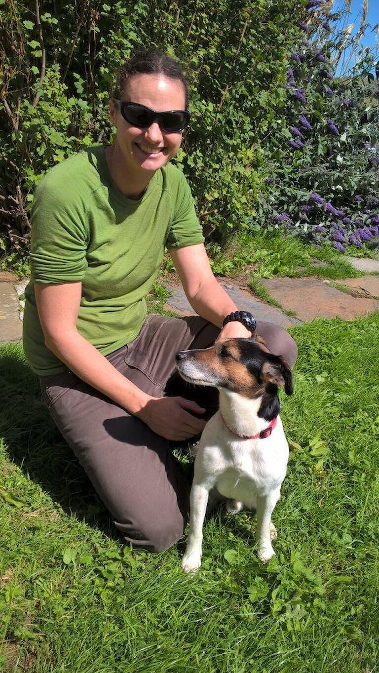 Women kneels by small dog in garden