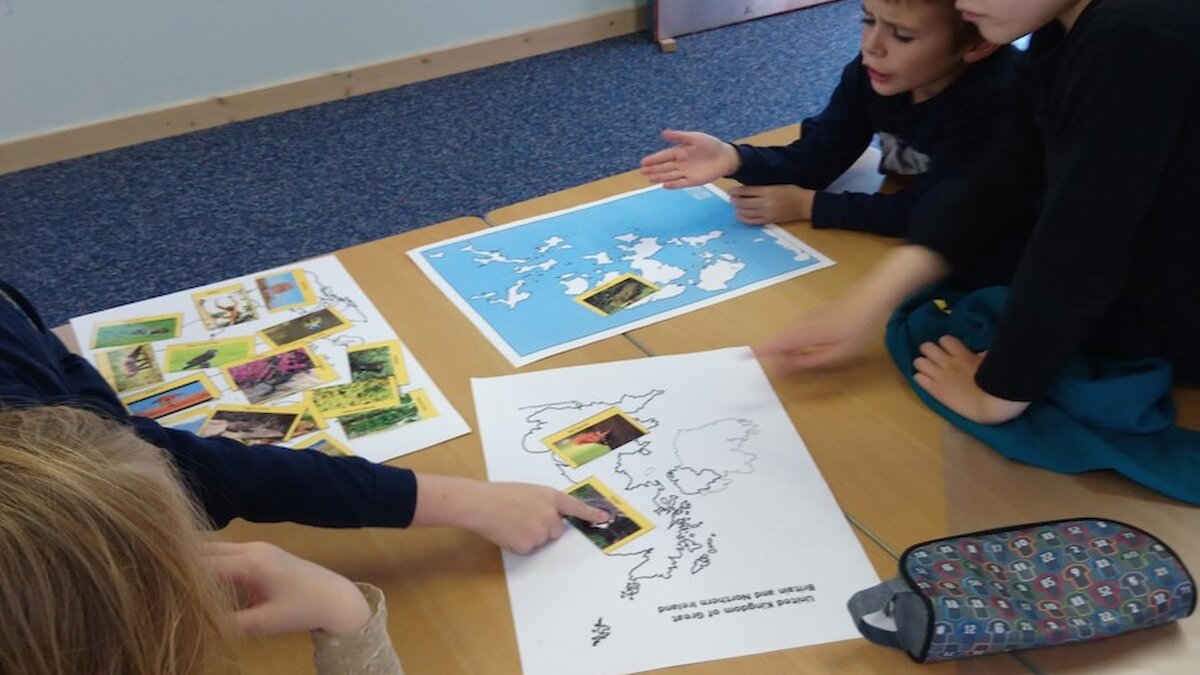 Children look at map and picture cards on a desk
